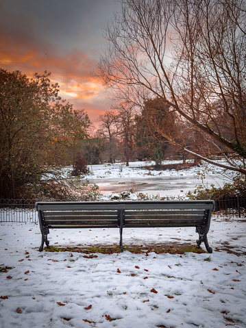 Frozen london city park pond and bench with rich cloudy sunset sky