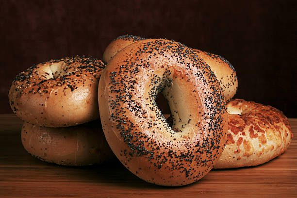 Bagel Group "group of bagels - poppyseed, garlic, and cheese - on a cutting board" poppy seed bagels stock pictures, royalty-free photos & images