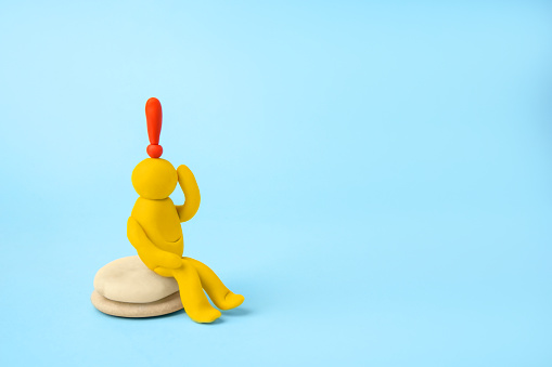 Human figure made of yellow plasticine with exclamation mark as solution idea on light blue background. Space for text