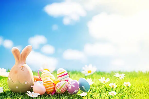 Photo of Easter bunny and eggs on meadow with cloudy sky background