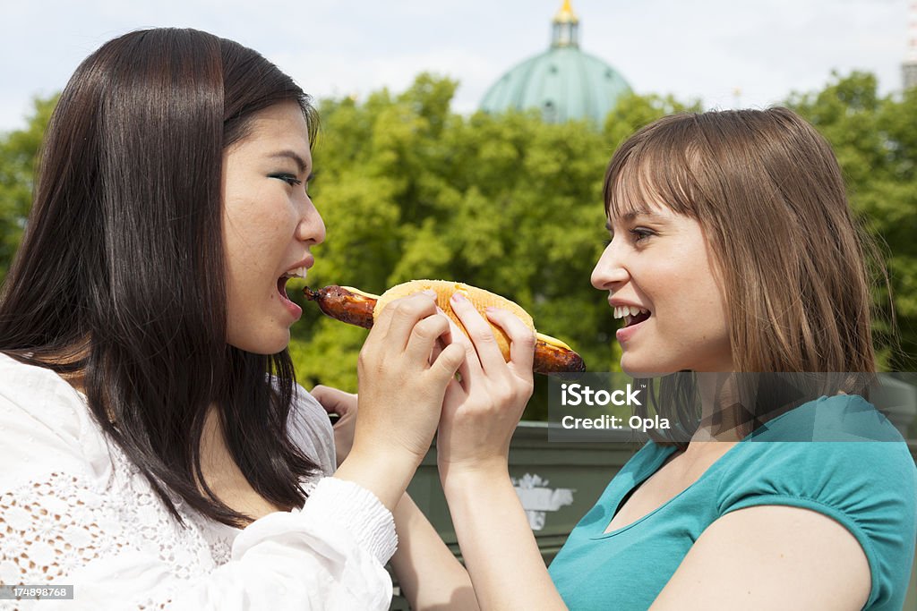 Two young women sharing a sausage roll 20-24 Years Stock Photo