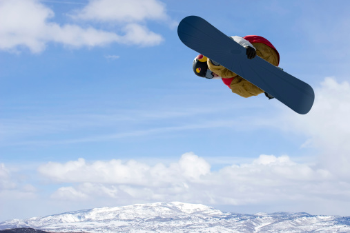 Snowboarder goes big against a beautiful blue sky and snow covered mountains in background. Room for copy.