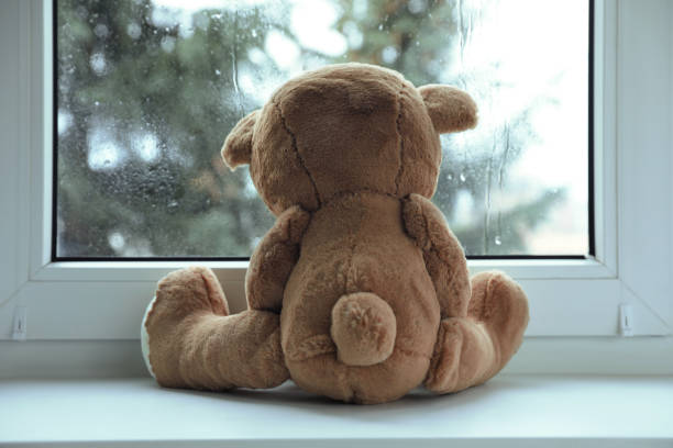 istock Cute lonely teddy bear on windowsill indoors, back view 1748988694