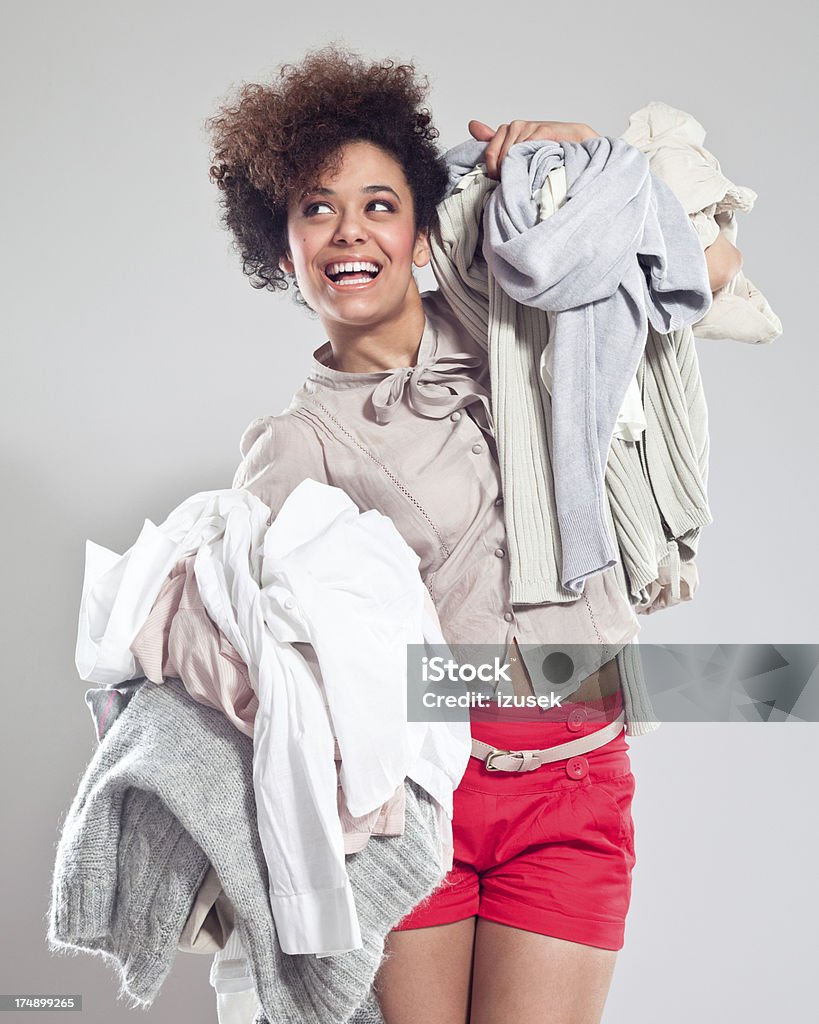 Happy Young Woman carrying clothes Portrait of beautiful teenaged afro girl carrying two piles of clothes in her hands, looking away and smiling. Laundry Stock Photo