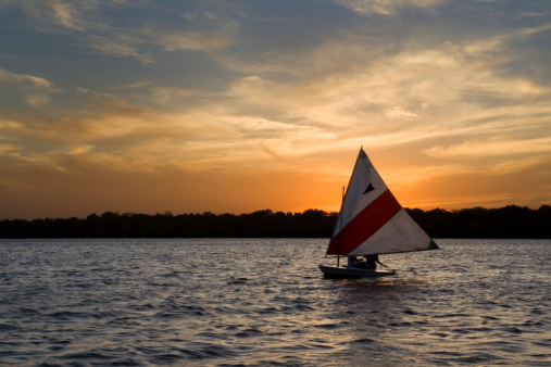 Single sailboat, a nautical vessel sailing at sunset on Lake Harriet, Minneapolis, Minnesota, USA