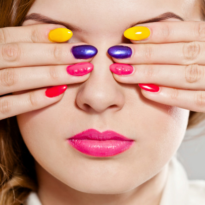 Close up of young woman covering her eyes by hands with multicolored manicure. Studio shot.