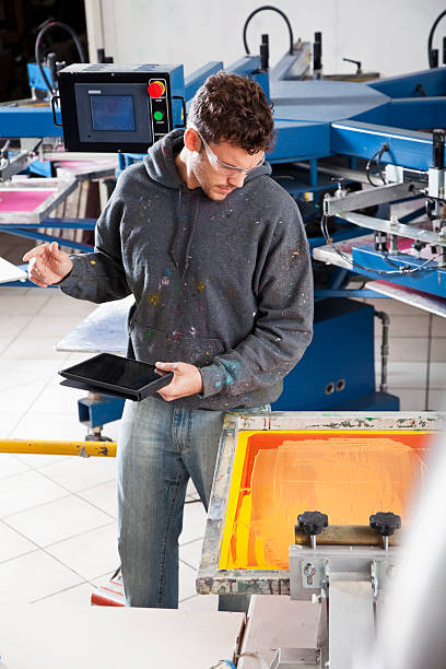 homem trabalhando na loja de impressão de tela - young men printing plant printing press factory - fotografias e filmes do acervo