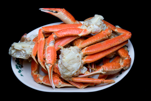 cooked crab legs on a plate. Black background.