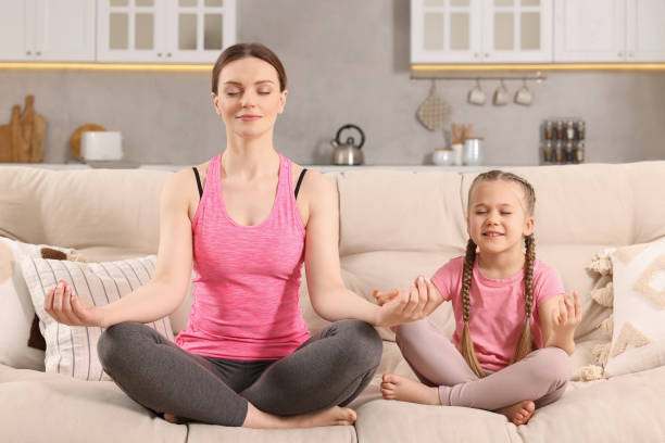 istock Mother with daughter meditating on sofa at home. Harmony and zen 1749040529