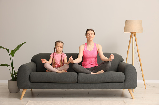 Mother with daughter meditating on sofa at home. Harmony and zen