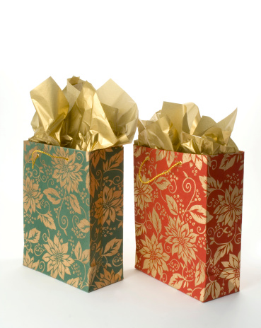 Two christmas gift bags with gold tissue paper, side by side on a white background. They are fancy, wrapped red and green holiday presents for a special celebration.