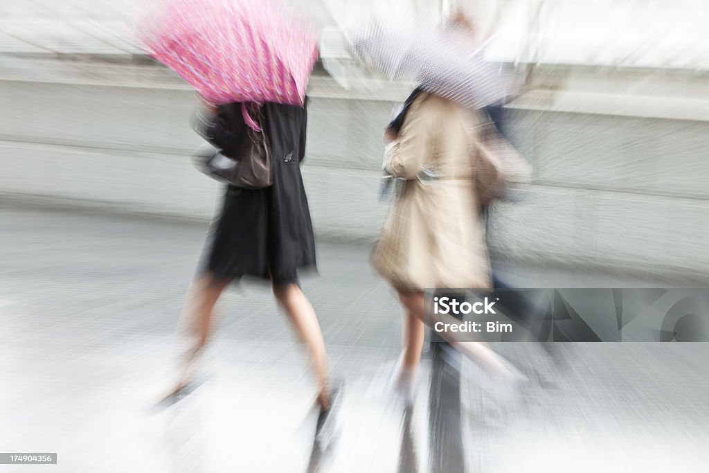 Two Young Women Walking with Umbrellas in Rainy Day, London two young women with umbrellas and one man walking in rainy day along Thames riverside, London, United Kingdom, Rain Stock Photo