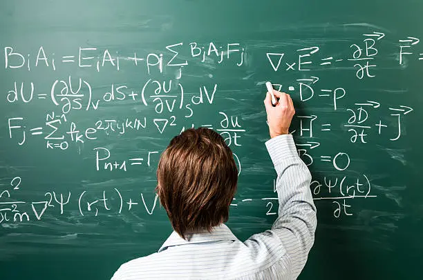 "Newton's Equations. Close-up on young man standing back against green chalkboard. He explains, solves physics tasks."