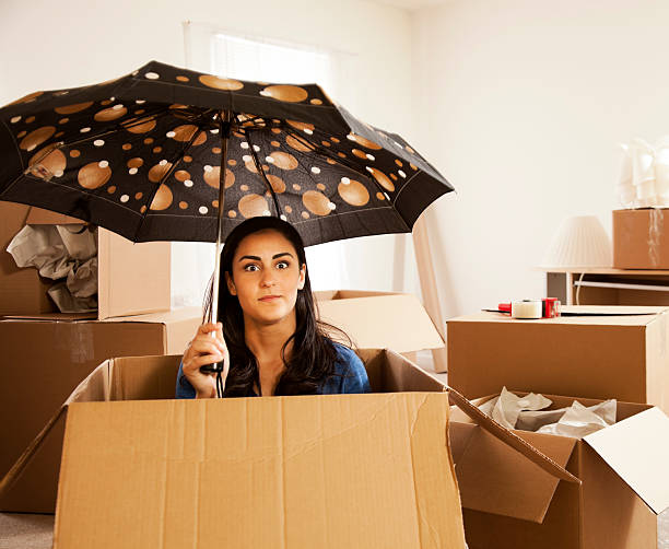 Moving Day with a Chance of Rain A young girl sits inside a moving box holding an umbrella. unpacking photos stock pictures, royalty-free photos & images