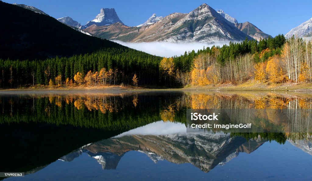 Beautiful Canadian Rockies Reflection Wedge Pond in the Canadian Rockies. Singh Ray warming polarizer to enhance the beautiful fall colours. This image taken in the Kananaskis region of Alberta in autumn. A perfect still morning with some fog allowed for the idyllic reflection in this famous pond. Wedge Pond is one of the most popular spots for nature photographers in Calgary. Image taken with Canon 5D Mark II camera.  Alberta Stock Photo