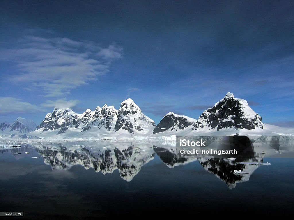 Deep Blue Antarctica Stunning mountain range in Neumeyer Channel in Antarctica. Snow and ice capped black mountains reflected in sea. Deep blue sky with some cloud. Small pieces of ice floating in sea in foreground. Taken with an Olympus C5060. Antarctica Stock Photo