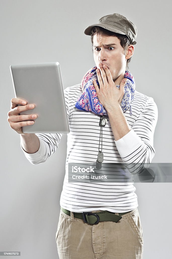 Young man using digital tablet Shocked young adult man using digital tablet. Studio shot, grey backgroound. 20-24 Years Stock Photo