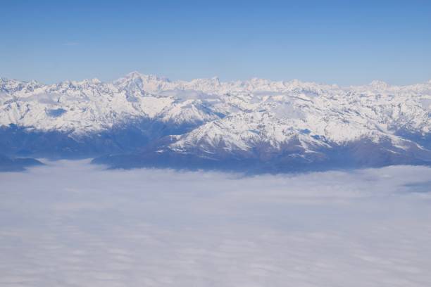 istock Alpine snowcapped mountains peaking through thick clouds with clear blue sky 1749078452