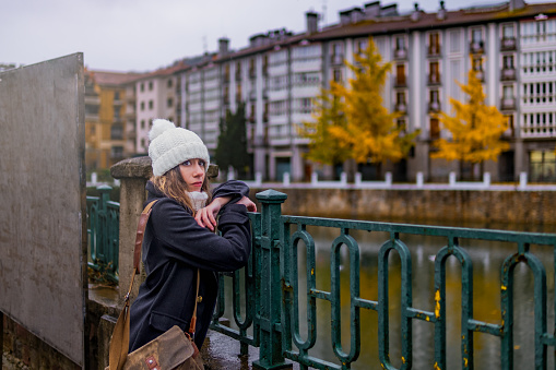 Half-length city portrait of a young female traveler posing on a railing in autumn. Tolosa, Spain.