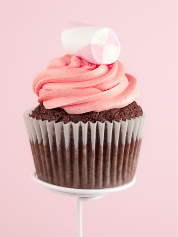 Delicious cupcake topped with buttercream and Marshmallow candy. Pink background.