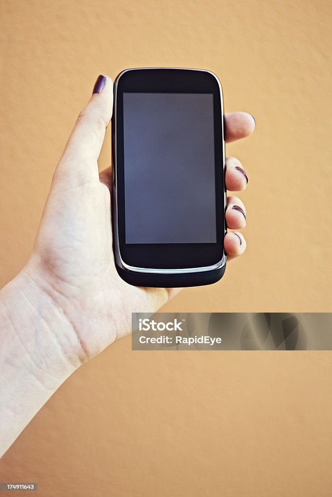 Female hand holding up smart phone, screen providing copy space "A woman's hand holds up a modern cellphone with an android operating system. The blank screen provides copy space, as does the tan background." Blank Stock Photo