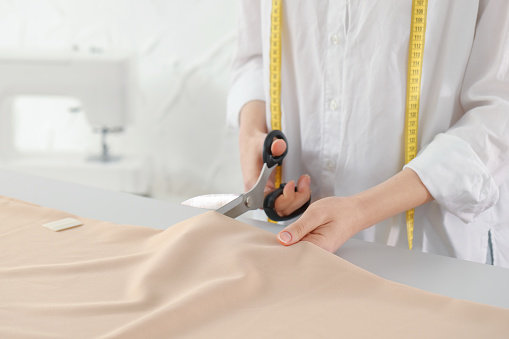 Dressmaker cutting fabric with scissors at table in atelier, closeup