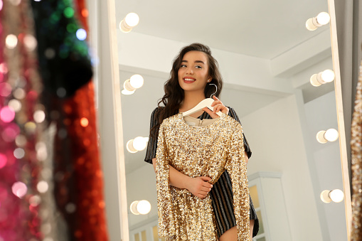 Beautiful young woman with golden sequin dress near mirror in boutique. Choosing party clothes