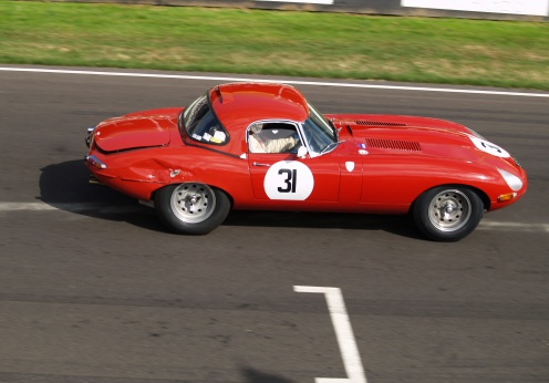 A slightly bent cat passes the start finish line. Red E type Jaguar