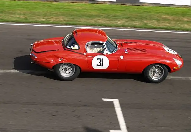 A slightly bent cat passes the start finish line. Red E type Jaguar