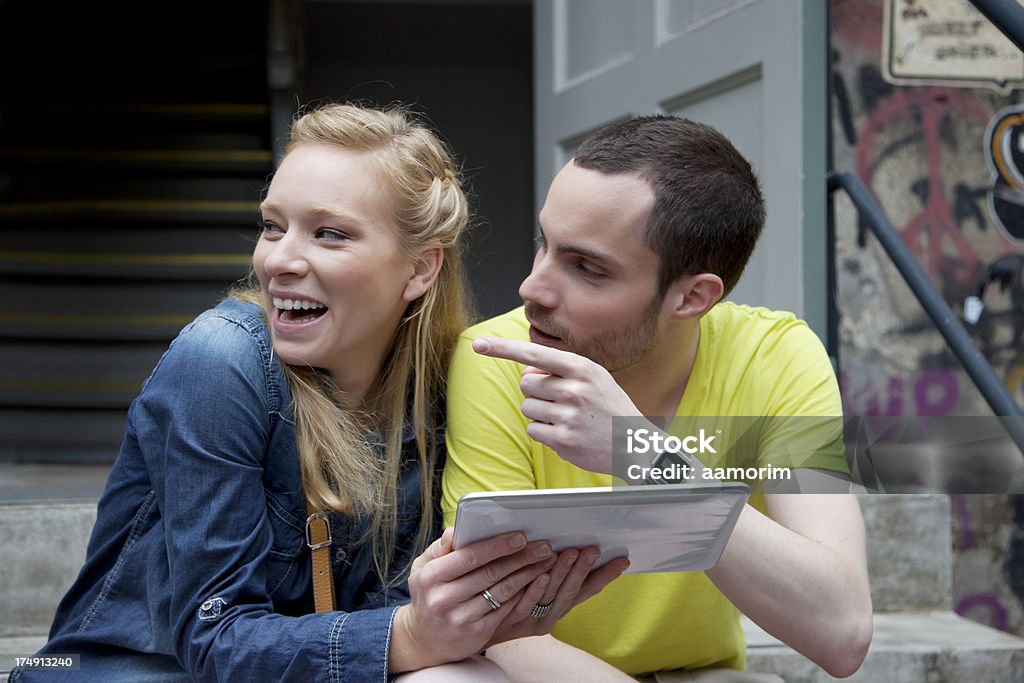 Young couple holding a Tablet "Young heterosexual couple holding a tablet. Both looking to the let, girl smiling and boy pouting at something." 20-29 Years Stock Photo