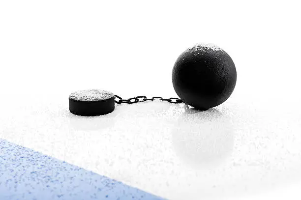 Concept of the NHL Lockout, with an idle hockey puck attached to a ball and chain covered in snow next to the Blue Line agaist a white background