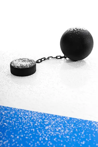 Concept of the NHL Lockout, with an idle hockey puck attached to a ball and chain covered in snow next to the Blue Line agaist a white background