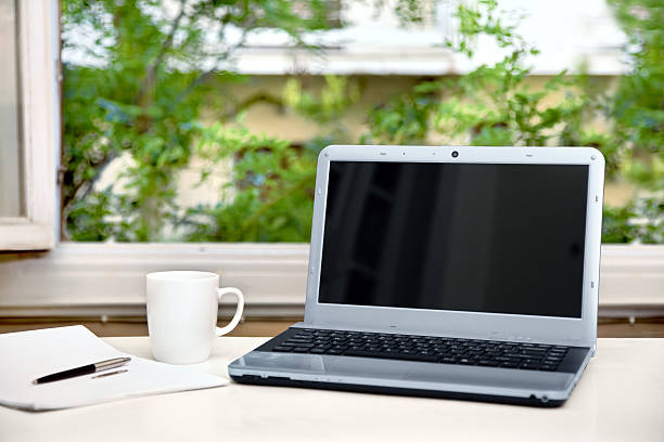 Laptop on desk in front of open window stock photo