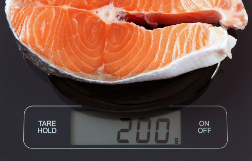 Steak of salmon fish in a black plate on digital scale displaying 200 gram.