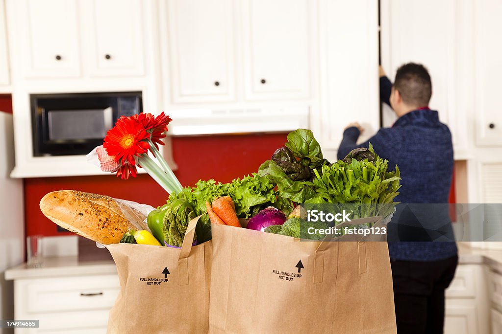 Cibo: Giovane latino uomo in cucina mette immediatamente Generi di drogheria verdure. - Foto stock royalty-free di Armadietto da cucina