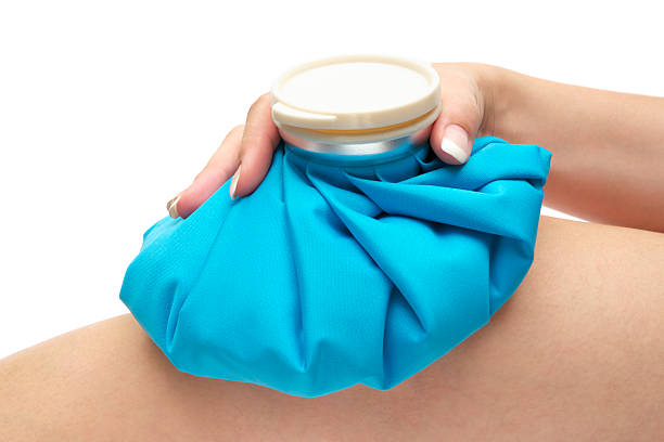 Ice Pack on Knee Woman cooling her injured knee with a blue ice pack. Isolated on a white background. physical therapy recovery touching human knee stock pictures, royalty-free photos & images