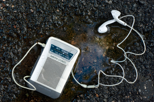 An old,worn FM stereo radio receiver with earphones, has fallen in a puddle.