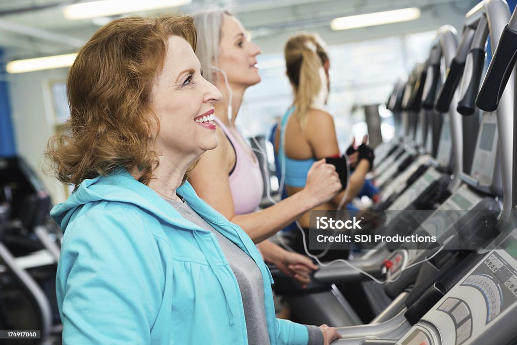 Ajuste mulher sênior exercitar-se na esteira na academia lotada - Foto de stock de 60 Anos royalty-free