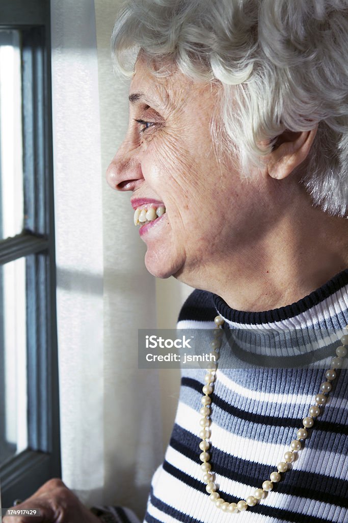 Mujer Senior sonrisas en la ventana - Foto de stock de 60-64 años libre de derechos