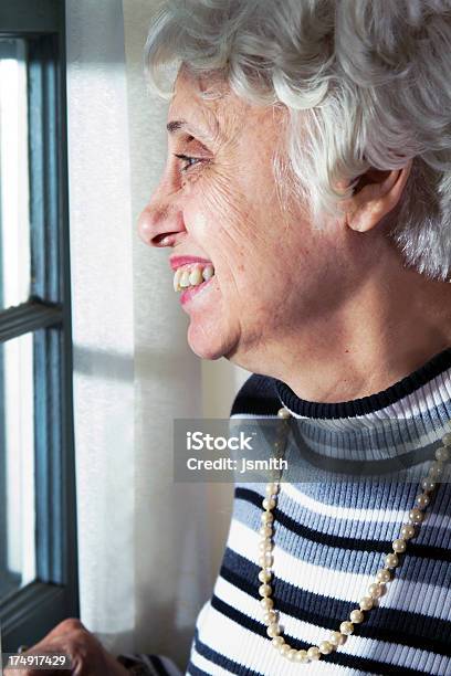 Mujer Senior Sonrisas En La Ventana Foto de stock y más banco de imágenes de 60-64 años - 60-64 años, 65-69 años, 70-79 años