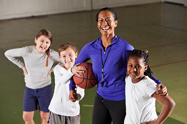 Girl's basketball team with coach Elementary school girls (7-8 years) on basketball team, standing in gym with coach (30s).  Focus on African American girl and coach. basketball sport photos stock pictures, royalty-free photos & images