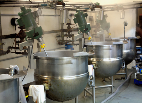 Industrial kitchen of a Candy factory with large stainless steel vats. Mixing and stirring hot candy.  Steam in background.