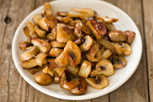 A high angle close up shot of a small white bowl full of sautAed mushrooms and onions. Shot on a grungy old wooden table