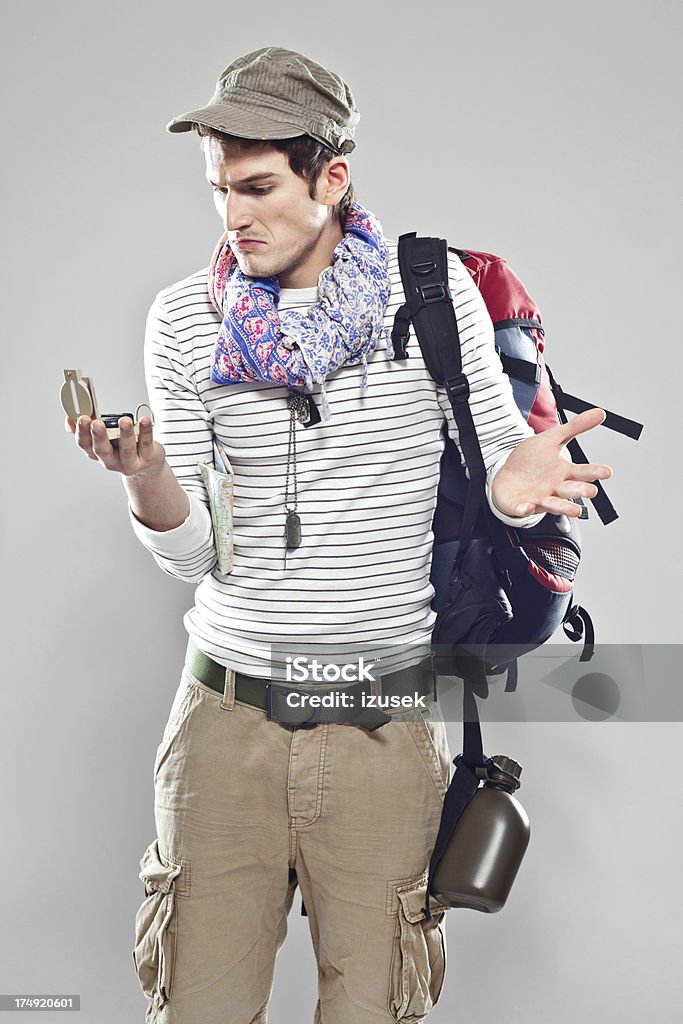 Confused male traveller Confused male backpacker looking at compass. Studio shot, grey backgroound. Holding Stock Photo