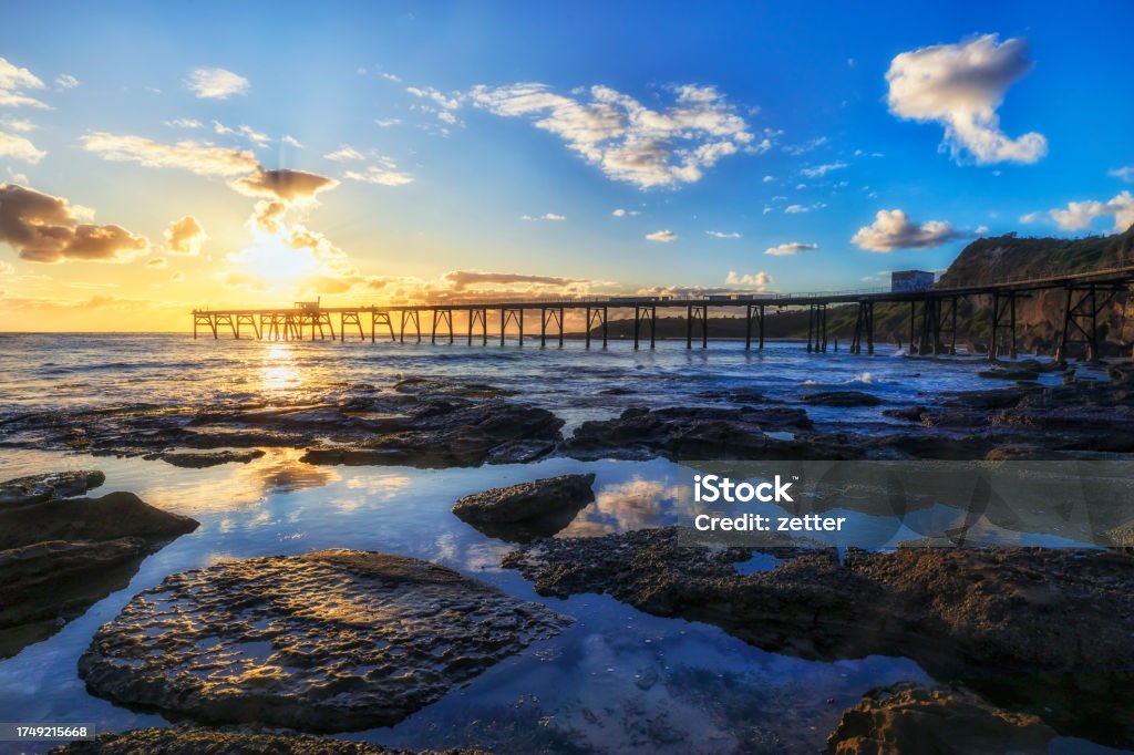 CHB Rocks pool reflects jetty Calm reflective waters on Middle camp beach of Australia on Pacific coast at sunrise near historic timber jetty. Australia Stock Photo