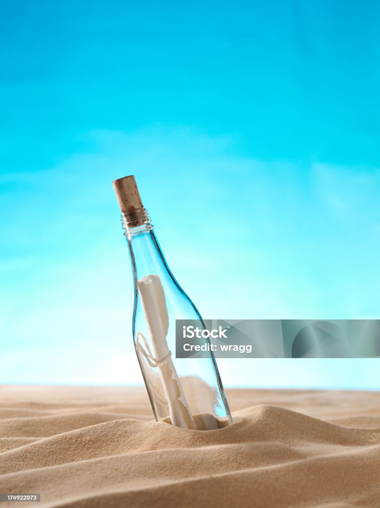 Message in a Bottle on the Sand Copy space on a blue paper background with message in a bottle on a sandy beach.Click on the link below to see more of my travel images. Bottle Stock Photo