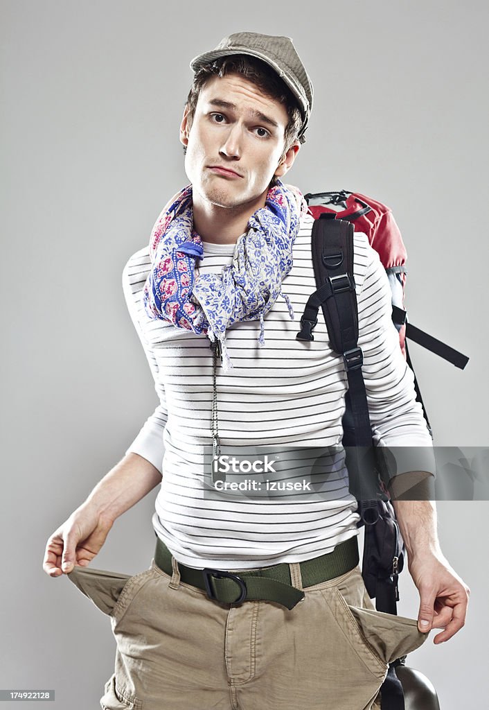 Poor traveller Young backpacker with empty pockets and no money looking at the camera. Studio shot, grey background. Empty Stock Photo