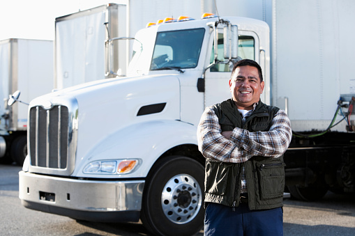 Hispanic truck driver (40s) standing in front of semi-truck.