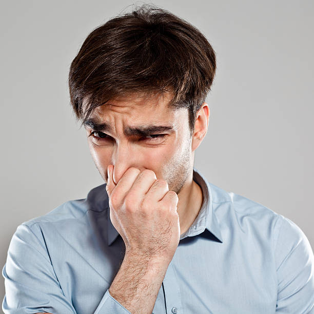 Man pinches nose Portrait of disgusted young man pinches his nose. Studio shot, grey background. frowning headshot close up studio shot stock pictures, royalty-free photos & images