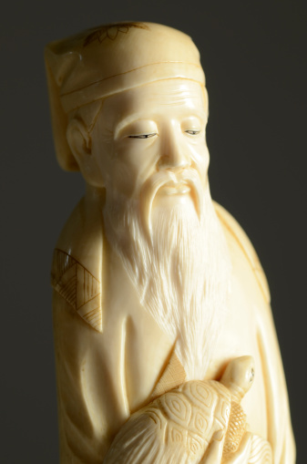 19th century Japanese carved ivory sculpture of an old man with a beard holding a turtle.  Looking right with a black background.